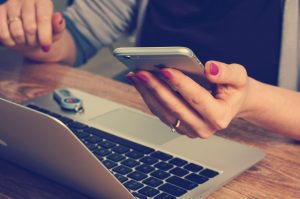 girl holding a phone near a laptop